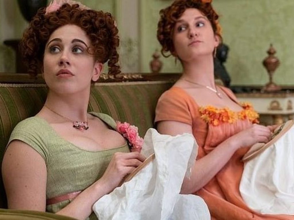 The older Featherington sisters, two white women with chestnut hair, seated on a sofa with their embroidery.