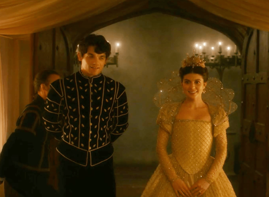 A screenshot of Jane and Guildford. He is wearing a black doublet with gold piping and embellishments. She is wearing a gold gown with a sheer, sparkly ruff.